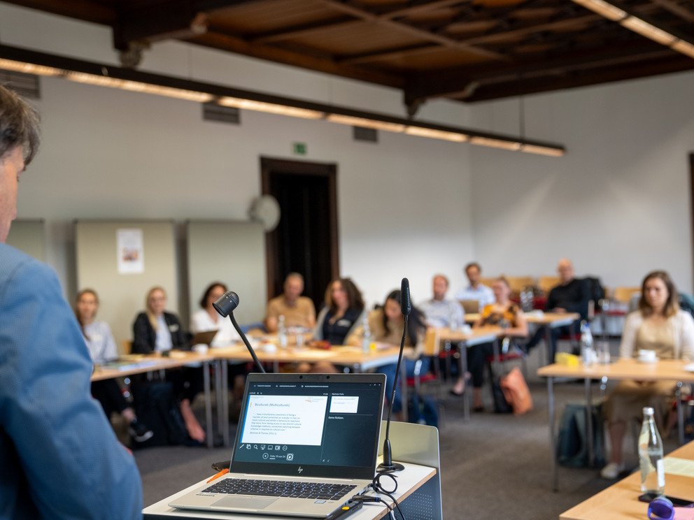 Speaker and laptop photographed from behind with participants in the background