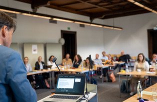 Speaker and laptop photographed from behind with participants in the background