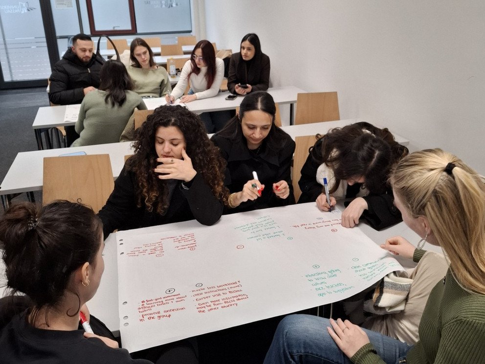 Studierende sitzen in Gruppen zusammen und arbeiten auf Flipcharts