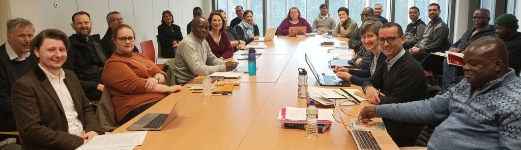 Seminarraum mit Fenstern; gr&ouml;&szlig;ere Gruppe von Studierenden und Lehrenden sitzt um einen runden Tisch