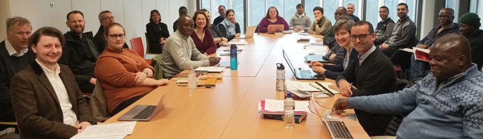 Seminarraum mit Fenstern; größere Gruppe von Studierenden und Lehrenden sitzt um einen runden Tisch