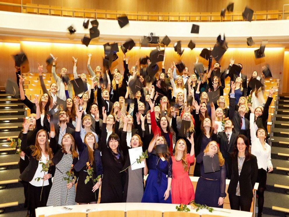 Students in the lecture hall toss their graduation caps in the air.