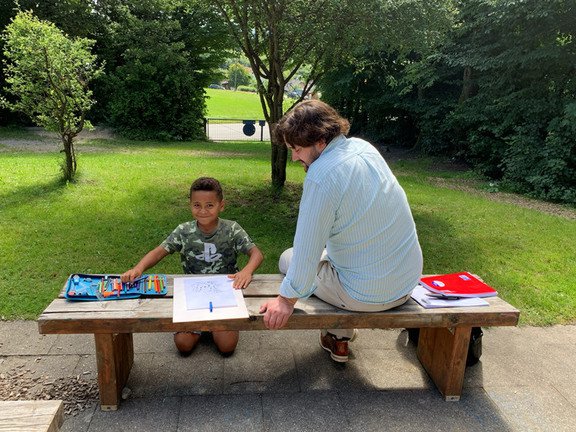 Mann sitzt auf einer Bank, kleiner sitzt vor der Bank und liest