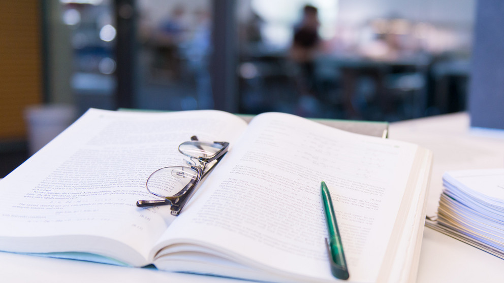 aufgeschlagenes Buch, darauf Brille und Stift